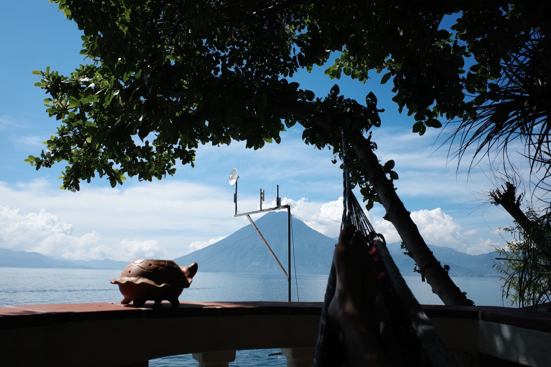 Feet up in a lakeside hammock on Lake Atitlán, a clay turtle on the wall and a volcano across the still water — the slow side of the lake.