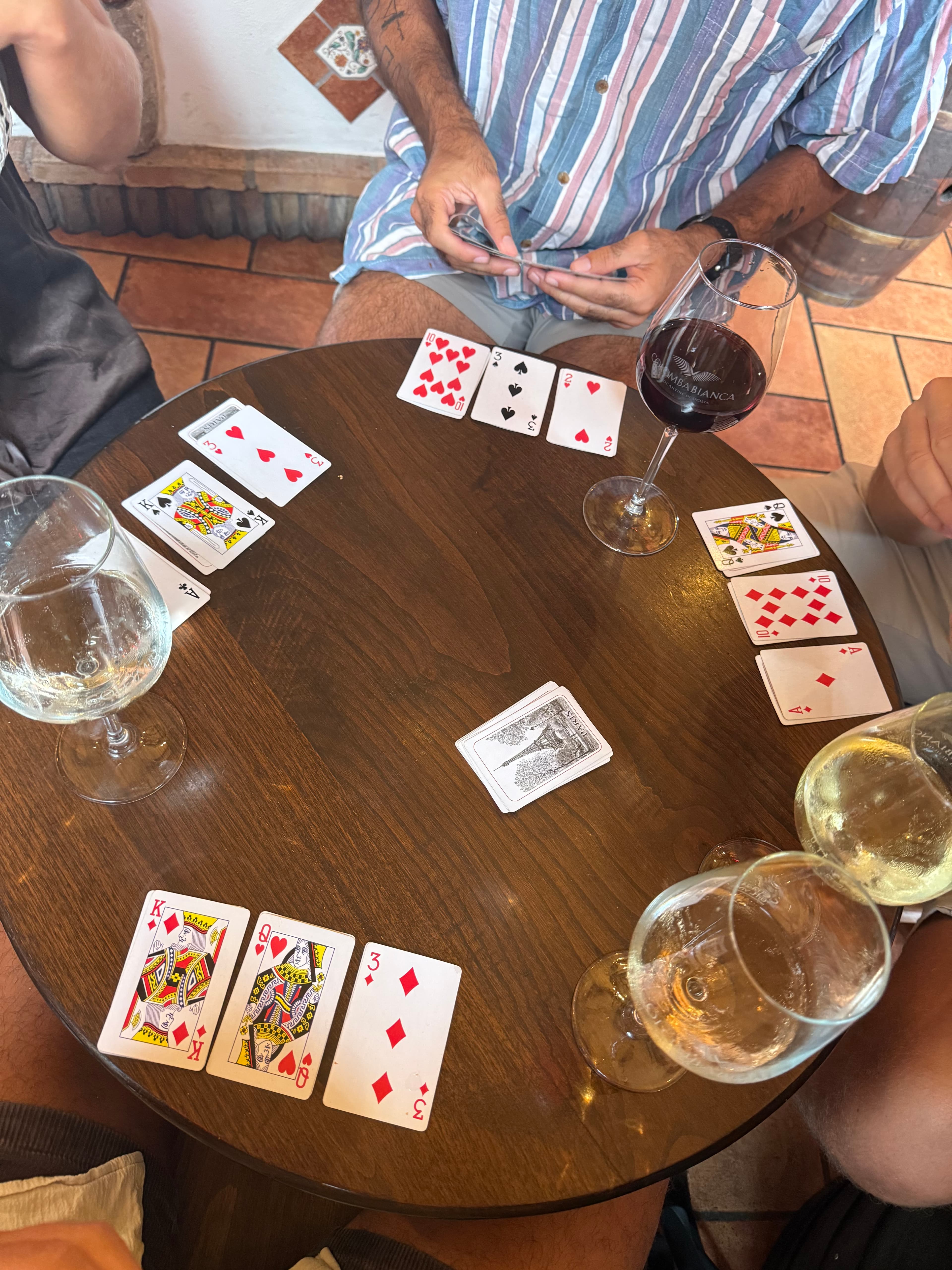 Italian aperitivo scene — wine glasses and hands of cards across a wooden tavolo, the kind of evening that makes Italy.