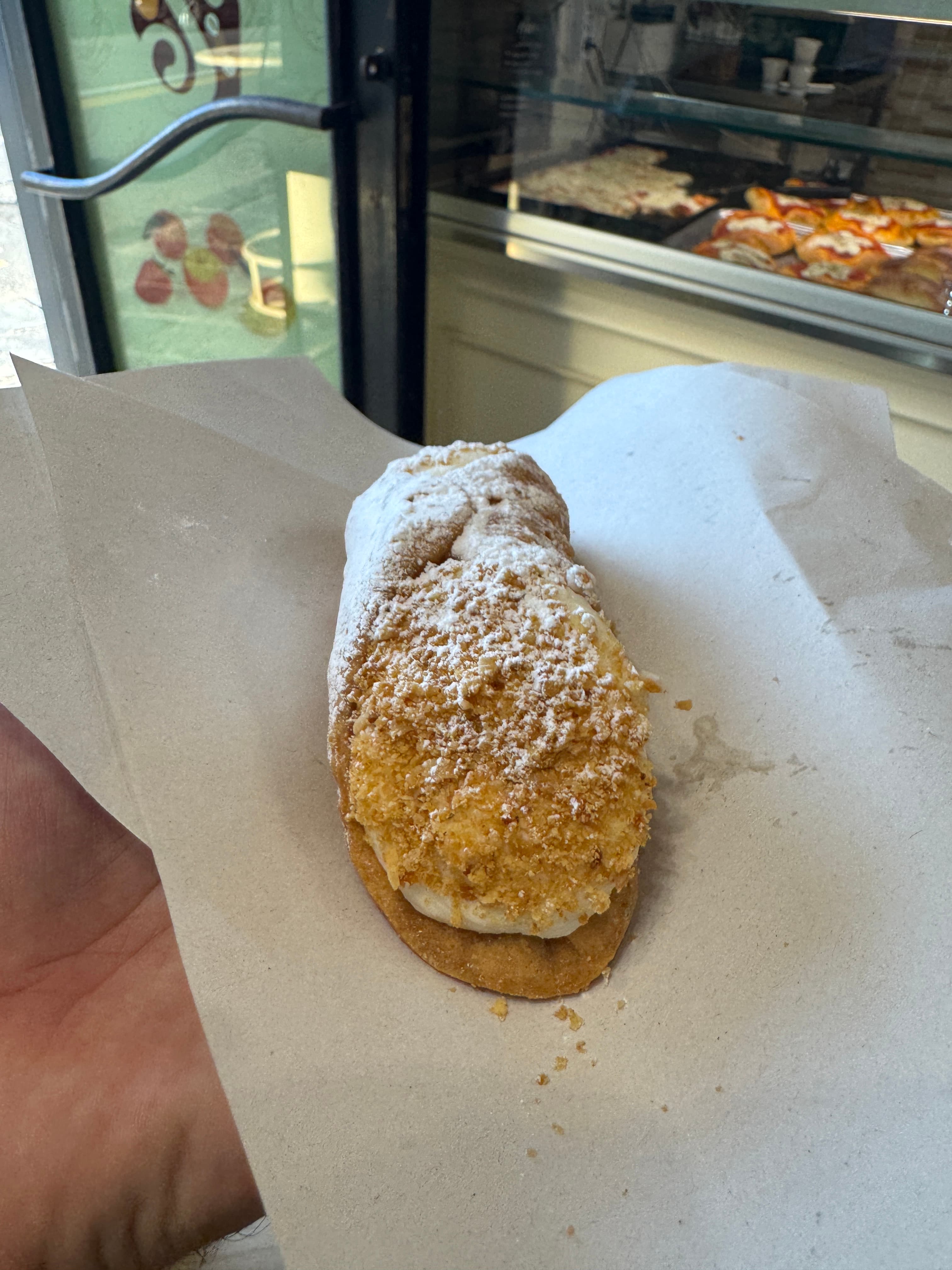 Sicilian pastry close-up at a Catania counter — powdered sugar dusted over filled dough, the kind of corner shop you'd walk past.