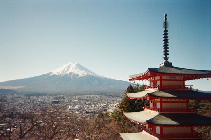 The Chureito Pagoda with snow-capped Mount Fuji behind it — the vermilion five-storey pagoda on the hill above Fujiyoshida, the perfect cone rising over the town in clear winter light.