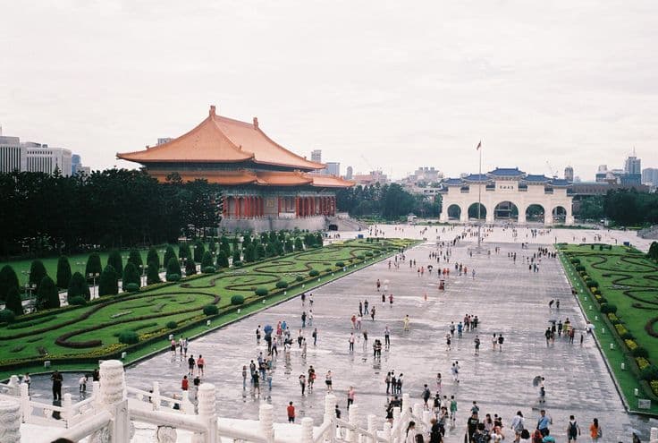 Liberty Square in Taipei — the National Theater's orange tiled roof to the left and the white Liberty Square gate in the distance, visitors and umbrellas scattered across the vast plaza.