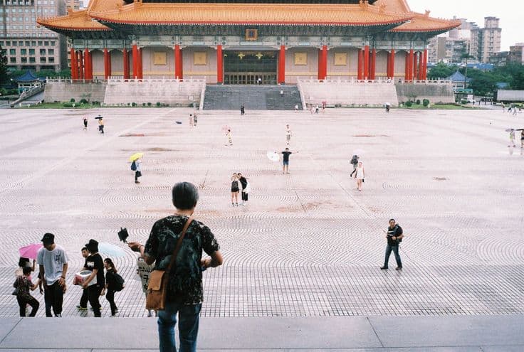 The National Concert Hall at Liberty Square, its ornate orange roof and red-columned facade rising over the huge patterned plaza, a street performer and scattered visitors below.