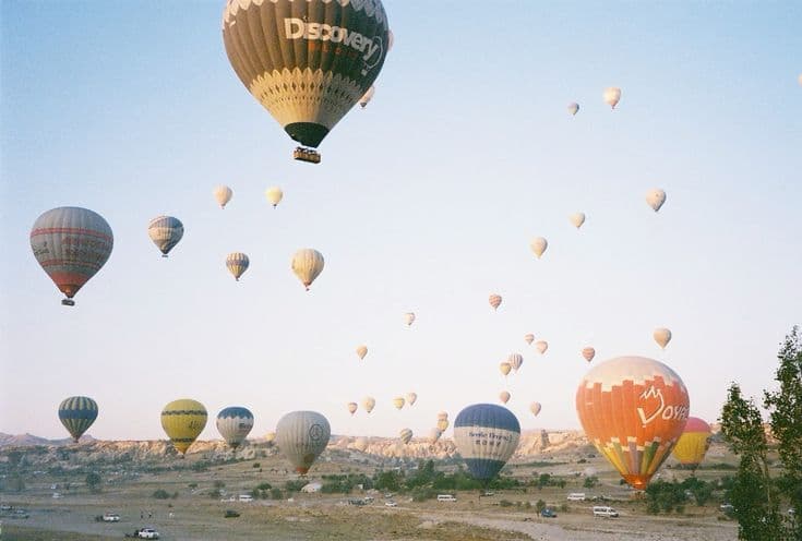 Sunrise over Cappadocia — dozens of hot-air balloons drifting over the Göreme valley at dawn, fairy chimneys and vineyards below.