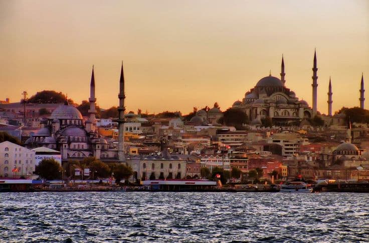Istanbul at golden hour — the domes and minarets of the Süleymaniye and the New Mosque glowing over the water as the sun sets.