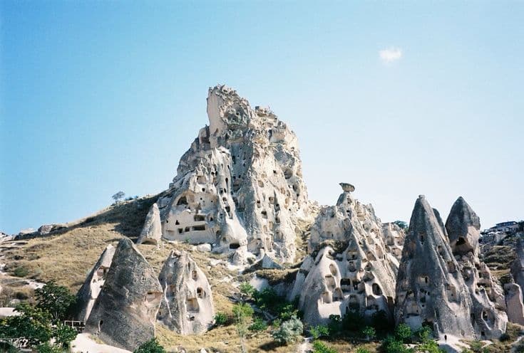 Uçhisar Castle in Cappadocia — a honeycombed rock fortress rising above fairy chimneys under a clear blue sky.