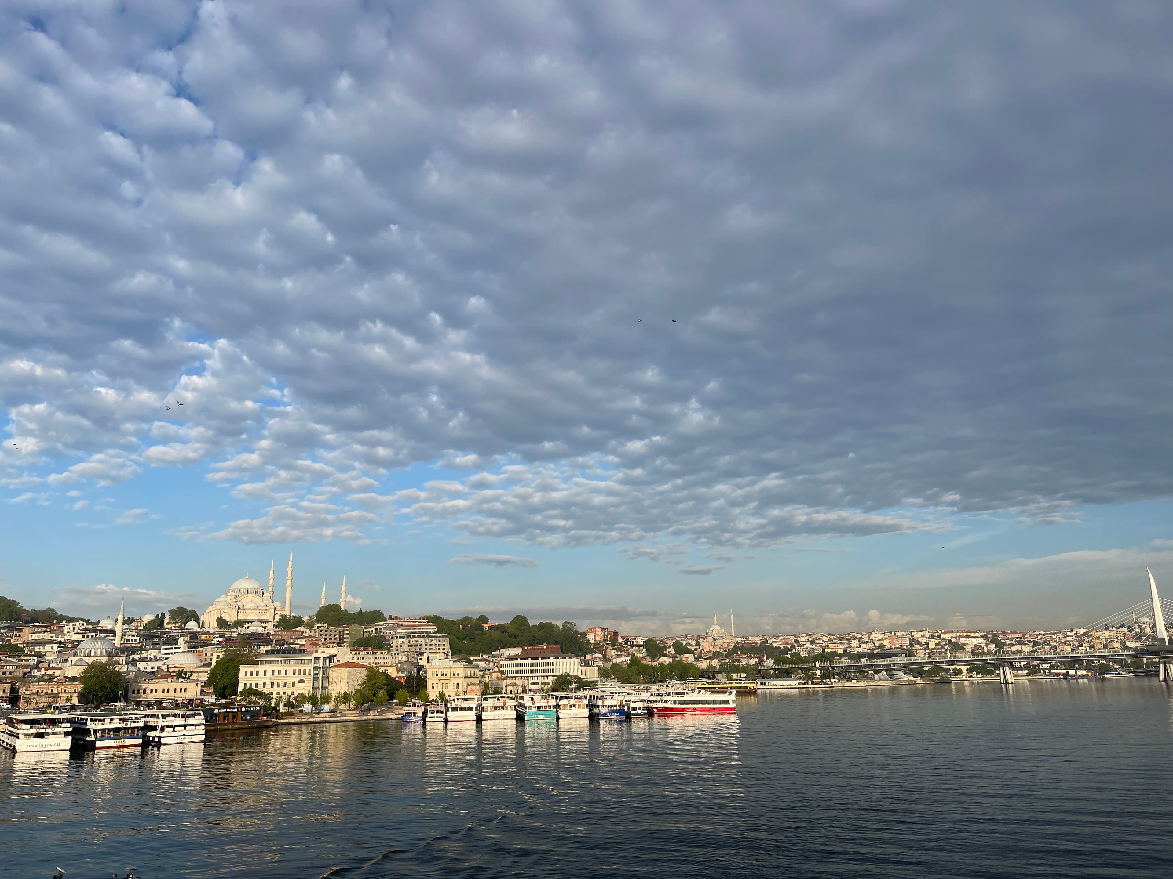 Istanbul across the Golden Horn — the Süleymaniye Mosque on the skyline, commuter ferries moored below a big cloud-streaked sky.