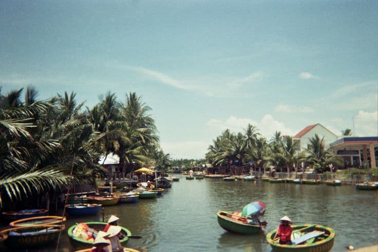 The round bamboo basket boats (thúng chai) of the Cẩm Thanh coconut village near Hoi An — paddlers in conical hats on a palm-lined river under a bright blue sky.
