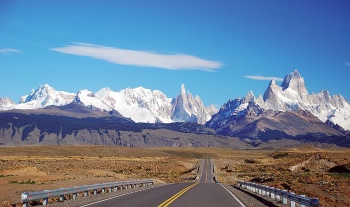 El Chaltén approach road with Fitz Roy and Cerro Torre in the distance — the granite spires of Patagonia at their most iconic.