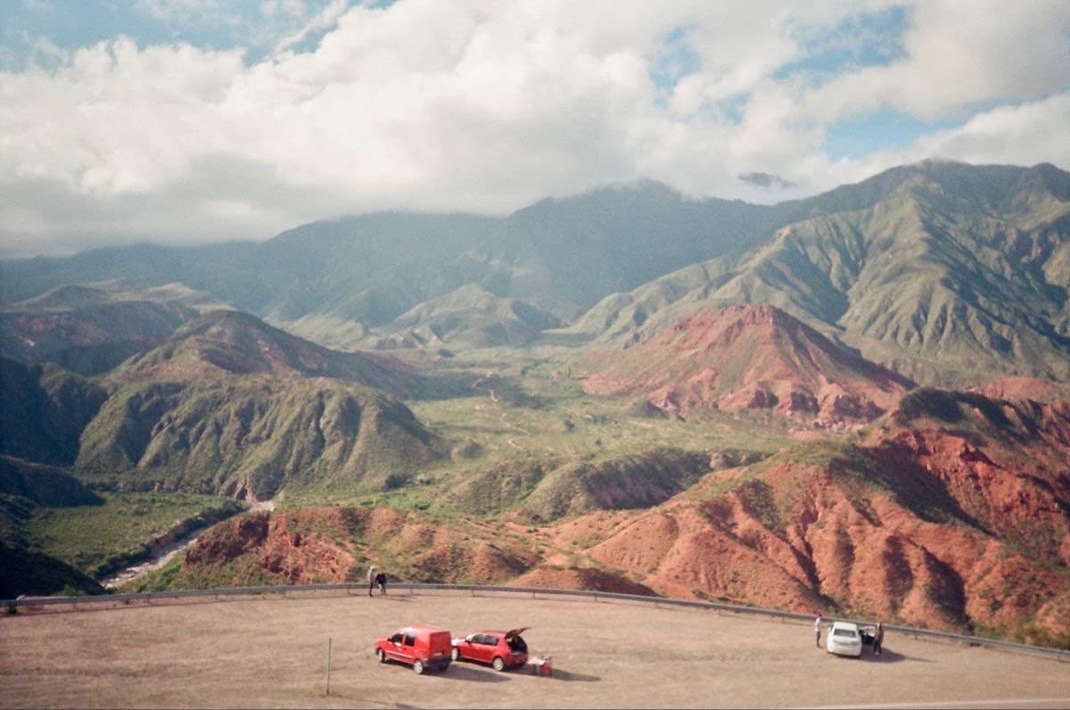 Cuesta del Obispo overlook in Argentina's northwest — red-earth valleys rolling into the Andes, a couple of cars parked on the ridge.
