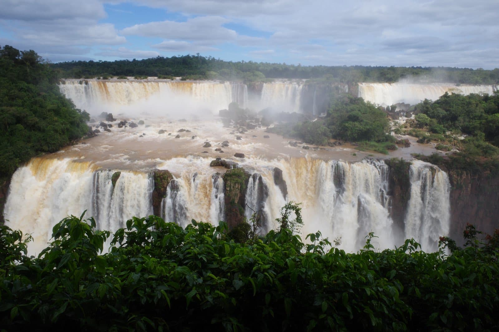 Iguazu Falls from the Brazilian side — the two-tier cataract dropping into jungle mist, curtains of water thundering into the Rio Iguaçu below.