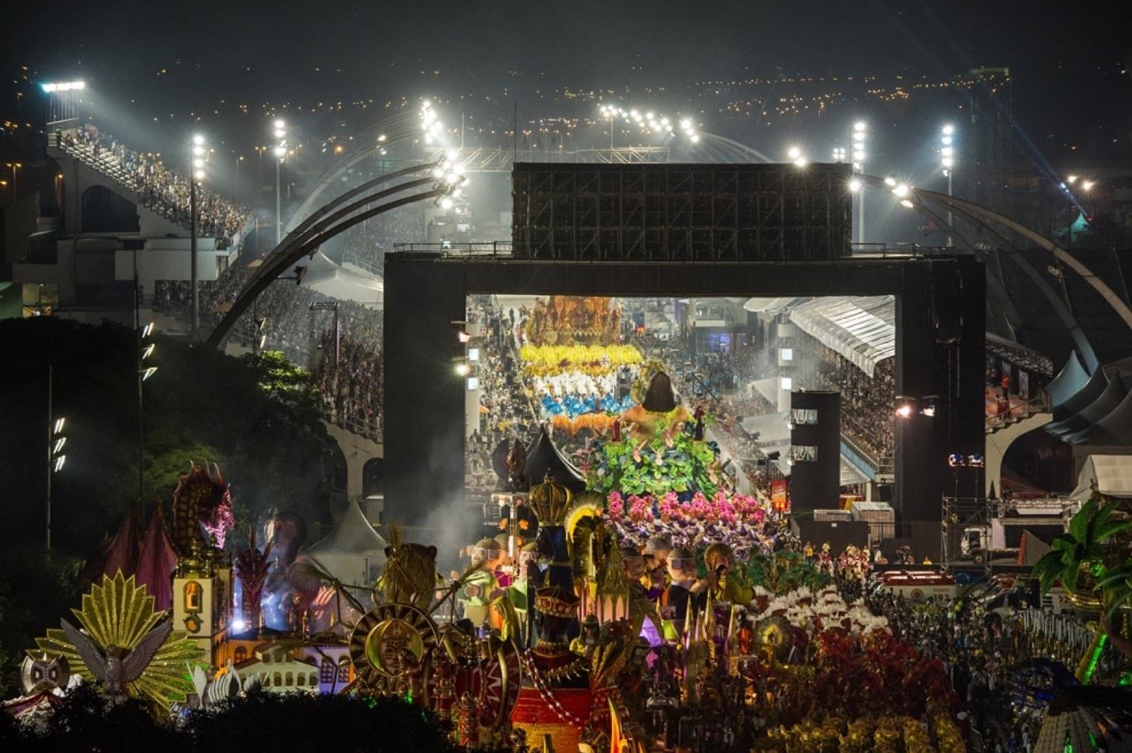 The Rio Carnaval at the Sambódromo — a lit-up samba-school float mid-parade, packed grandstands running the length of the avenue under stadium light.