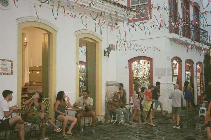 Salvador's Pelourinho — colourful Bonfim ribbons strung across a cobbled street of whitewashed colonial houses, people eating ice cream while a busker plays guitar.