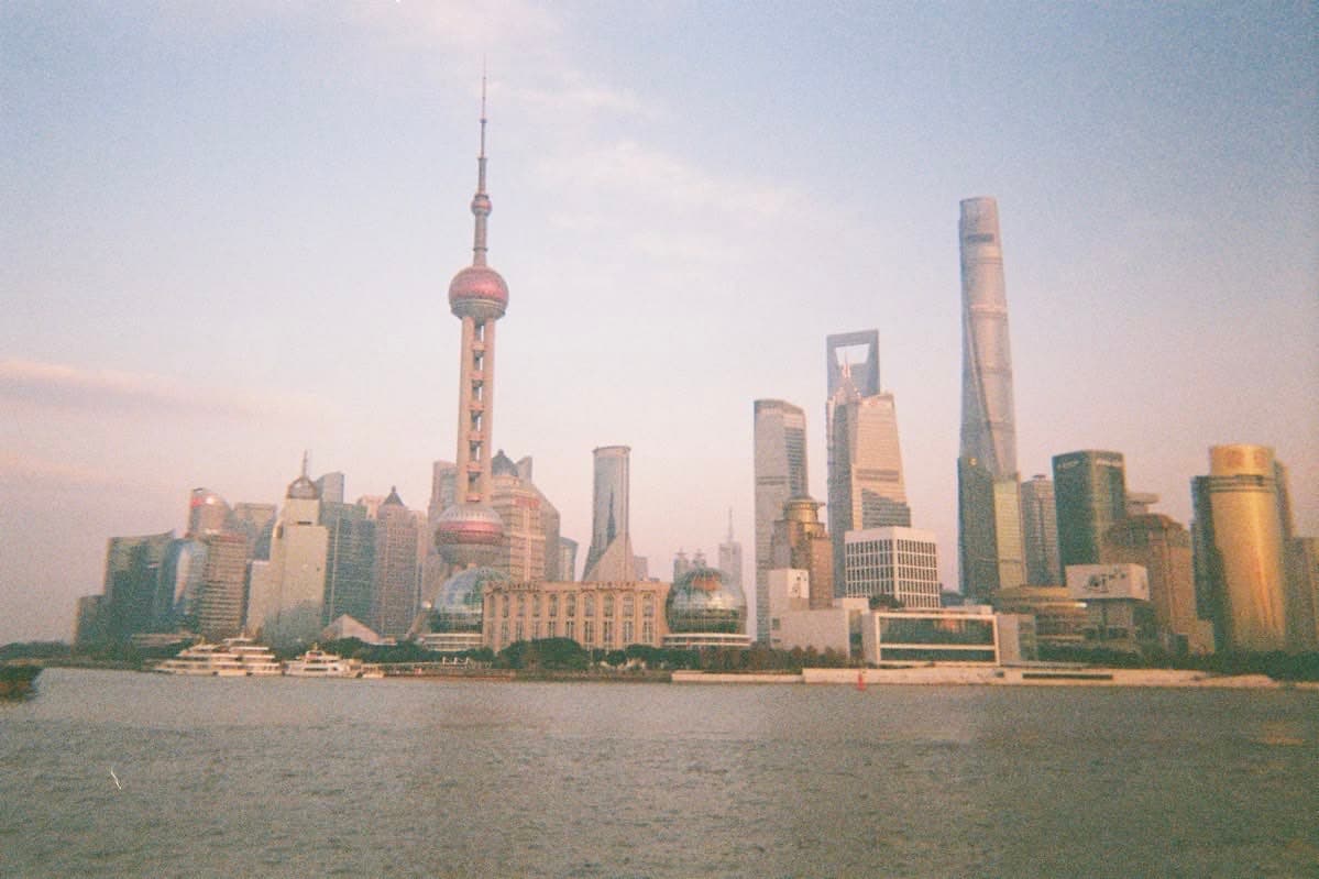 Shanghai's Pudong skyline from the Bund at sunset — the Oriental Pearl Tower rising over the Huangpu, Shanghai Tower and the World Financial Center behind.