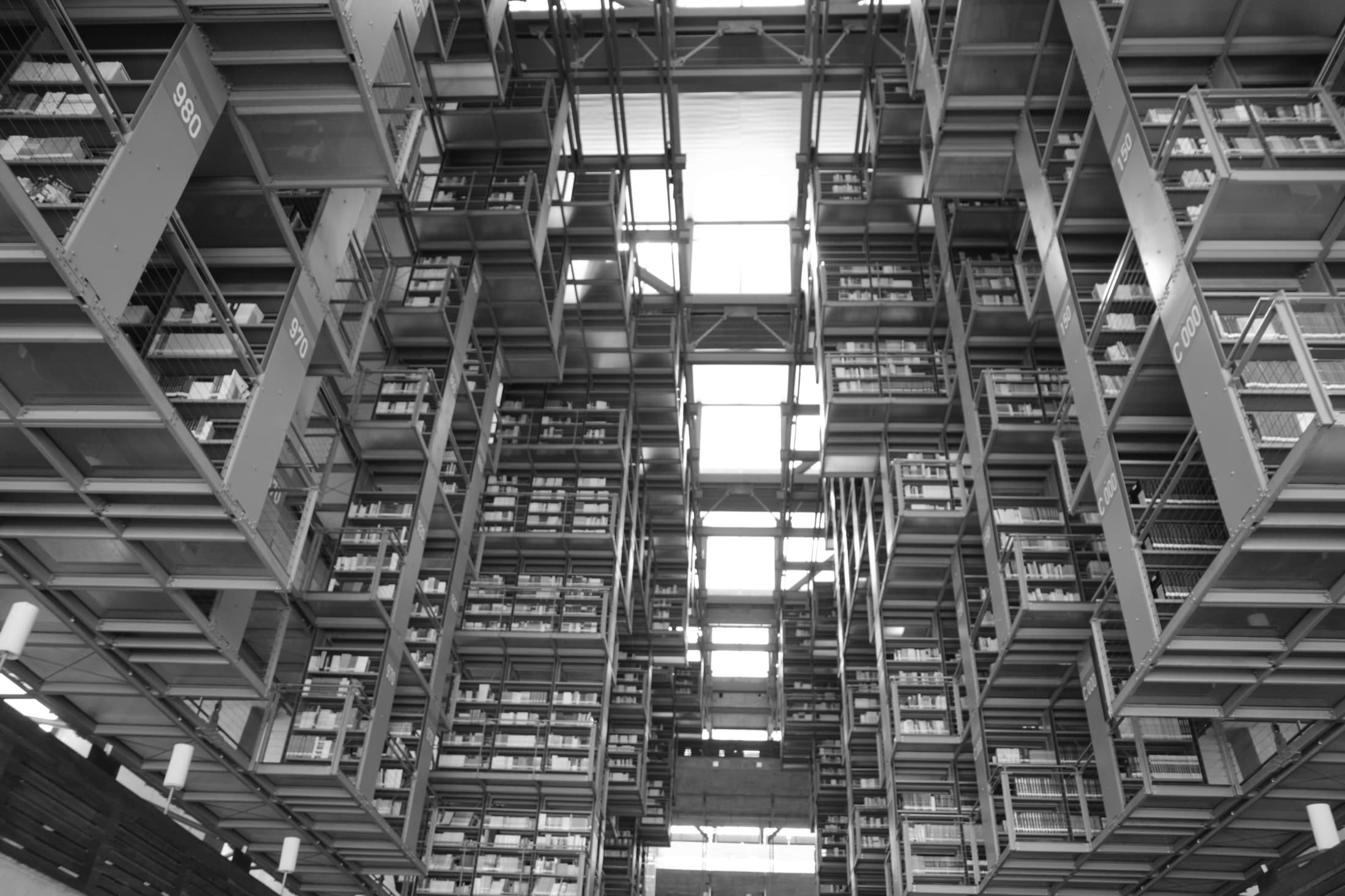 The cathedral-like interior of the Biblioteca Vasconcelos — floating steel book stacks receding under a glass roof, shot in stark black and white.