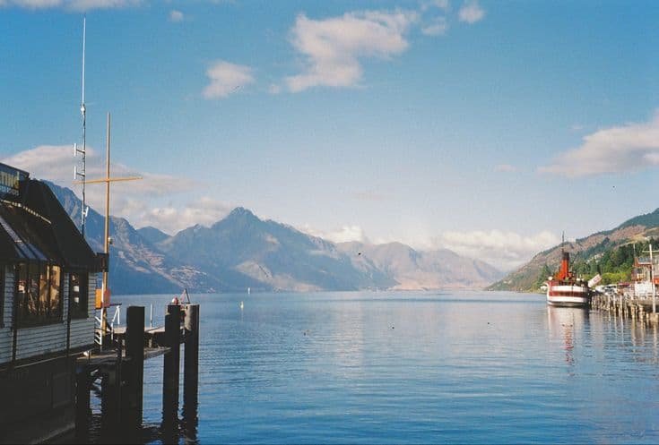 Lake Wakatipu at Queenstown — calm water reflecting the Remarkables, a jetty and the historic TSS Earnslaw steamship moored at the wharf on a bright morning.