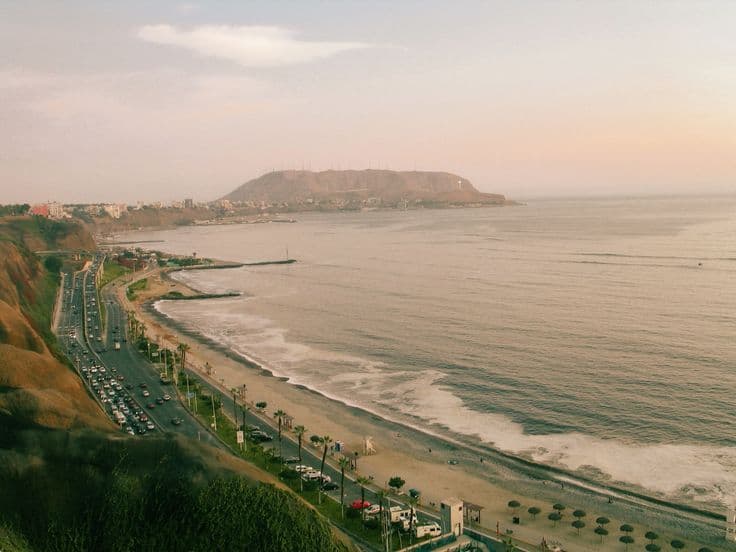 Lima's Costa Verde at dusk — the Miraflores clifftop road curving above the Pacific, the Morro Solar headland catching the last pink light.