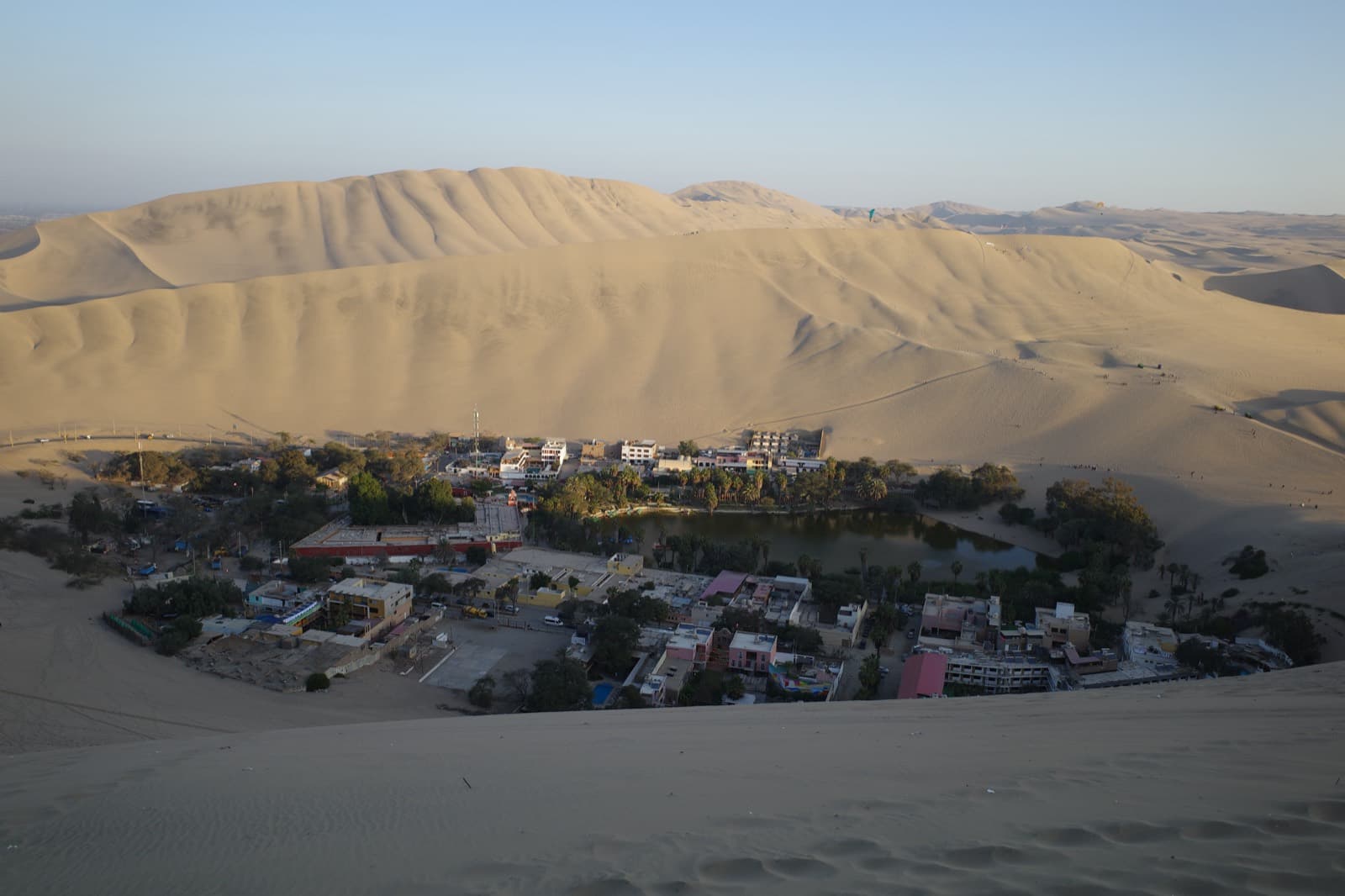 The Huacachina oasis near Ica — a palm-ringed lagoon and desert town encircled by towering sand dunes, sandboarders on the ridgelines.