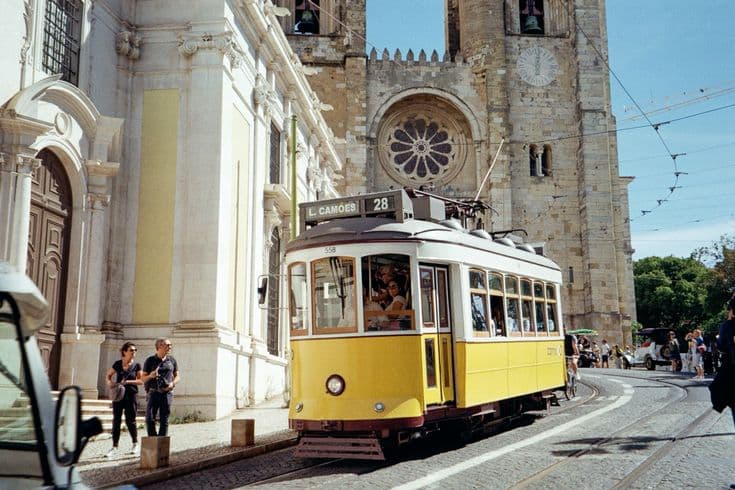 Lisbon's tram 28 — the classic yellow tram clattering past the rose window of the Sé cathedral in the old town.