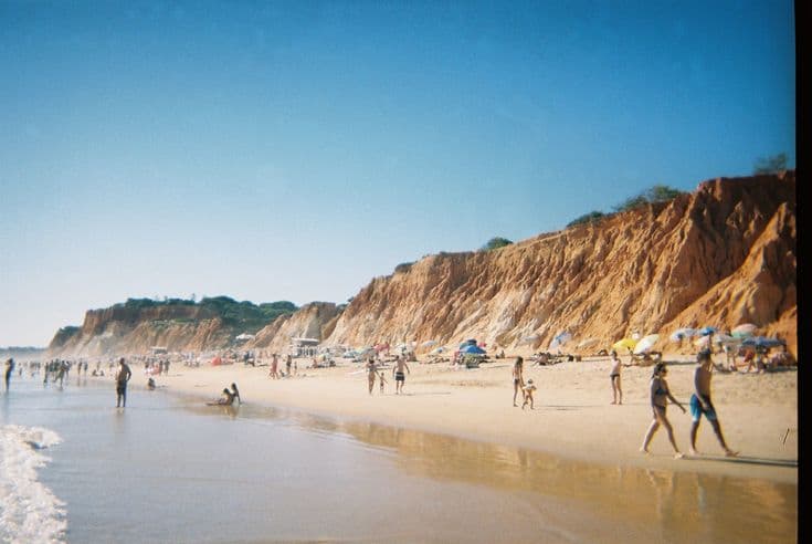 Praia da Falésia in the Algarve — golden sand backed by dramatic orange-and-ochre cliffs, sunbathers along the shoreline.