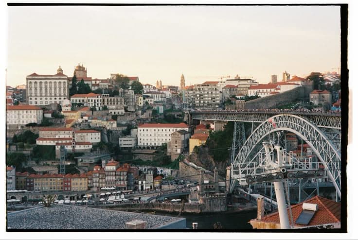 Porto at dusk — the tiled old town tumbling down to the Douro, the Dom Luís I iron bridge and the Gaia cable car in the foreground.